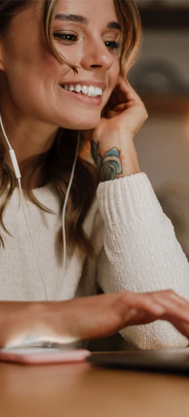 A woman wearing earphones, focused on her laptop